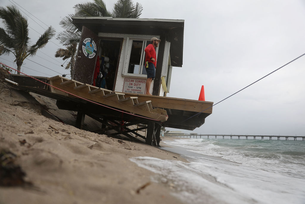 A Dania Beach lifeguard stands on his lifeguard stand that is in danger of being swept out to sea. Recent storms eroded the beach as municipalities try to figure out how to save the beaches as well as how to combat the consequences of sea level rise that threatens some of the coastal cities. (Credit: Joe Raedle/Getty Images)