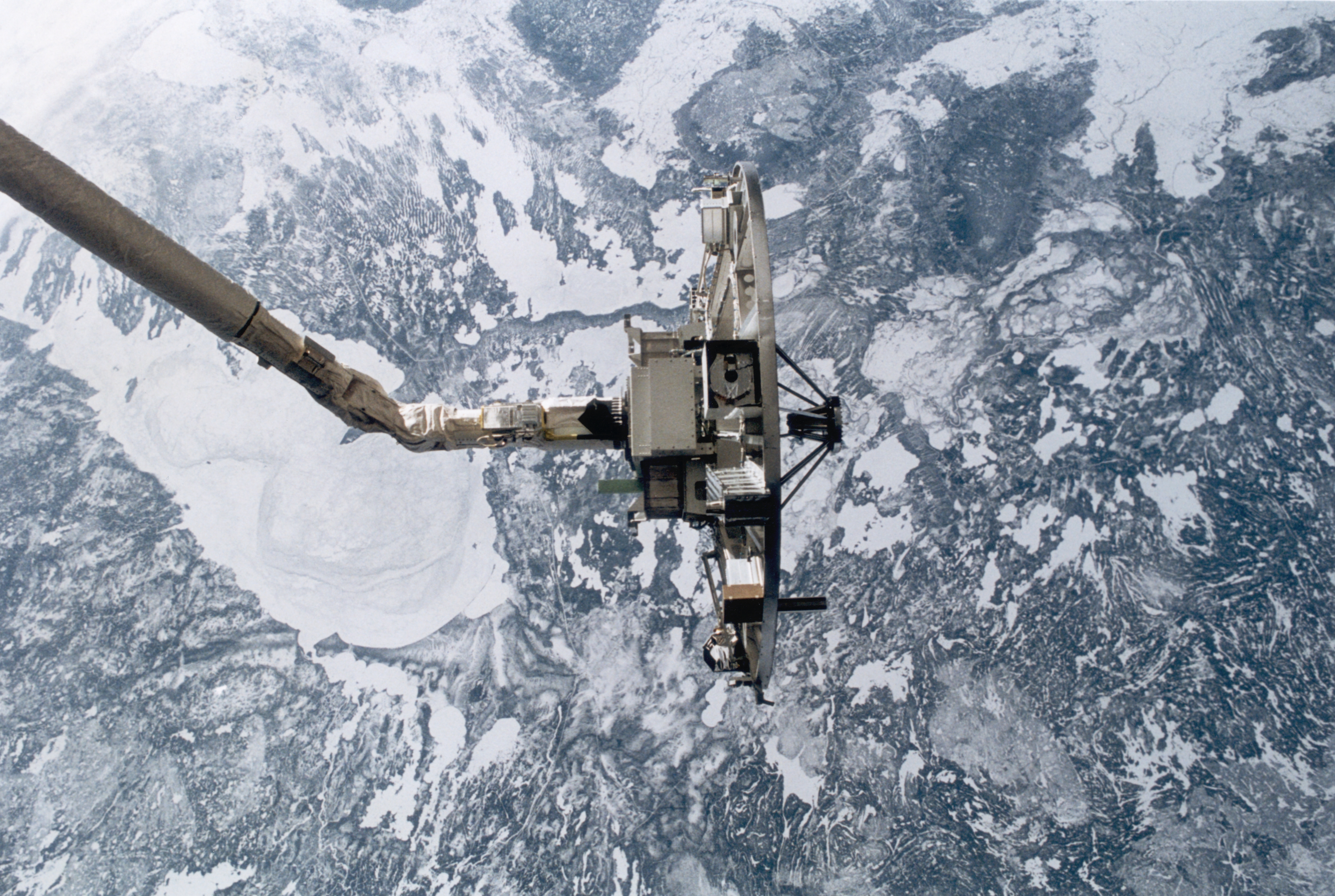 The Wake Shield Facility (WSF), an experimental science platform, positioned at the end of the Remote Manipulator System (RMS) on the space shuttle Discovery during NASA's STS-60 mission, February 1994. Behind the WSF is a wintry Lake Winnipeg in Manitoba. (Credit: Space Frontiers/Getty Images)