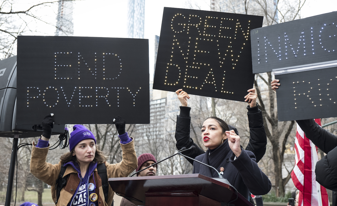 Rep. Alexandria Ocasio-Cortez (D-NY) speaks at 3rd Annual Woman's March in New York City on January 19, 2019. Signs behind her that say "End Proverty" and "Green New Deal". CREDIT: Ira L. Black/Corbis via Getty Images.