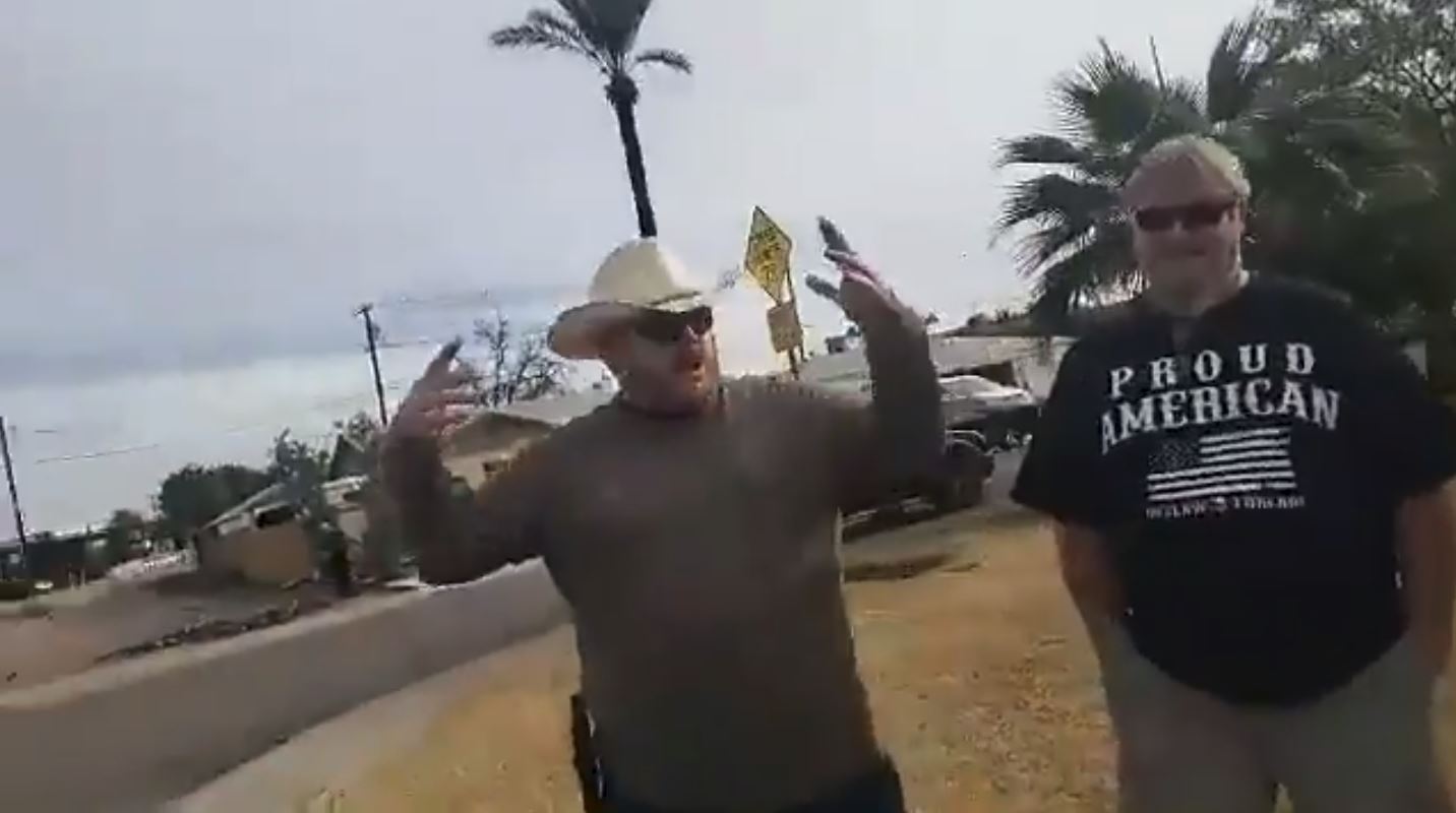 Two protesters affiliated with Patriot Movement Arizona (PMAZ) outside a church in Phoenix on Saturday, January 5. The man in the cowboy hat with the gun has just explained how he "busted right through the door" to confront staff inside. CREDIT: Screenshot/Nick Martin