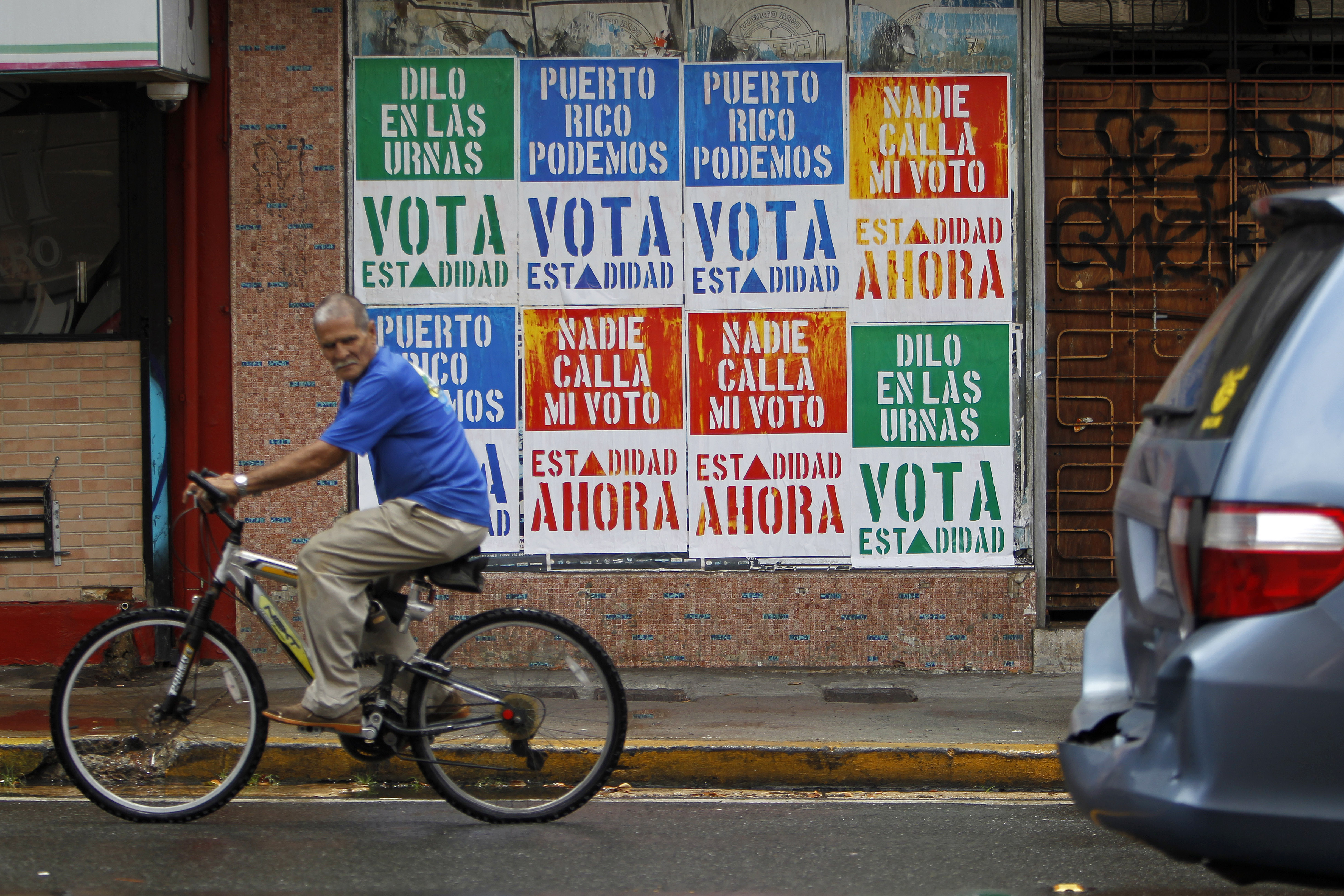 A man rides his bicycle in front of a wall covered with campaign posters promoting Puerto Rico's statehood in San Juan, on June 9, 2017. (Credit: RICARDO ARDUENGO/AFP/Getty Images)