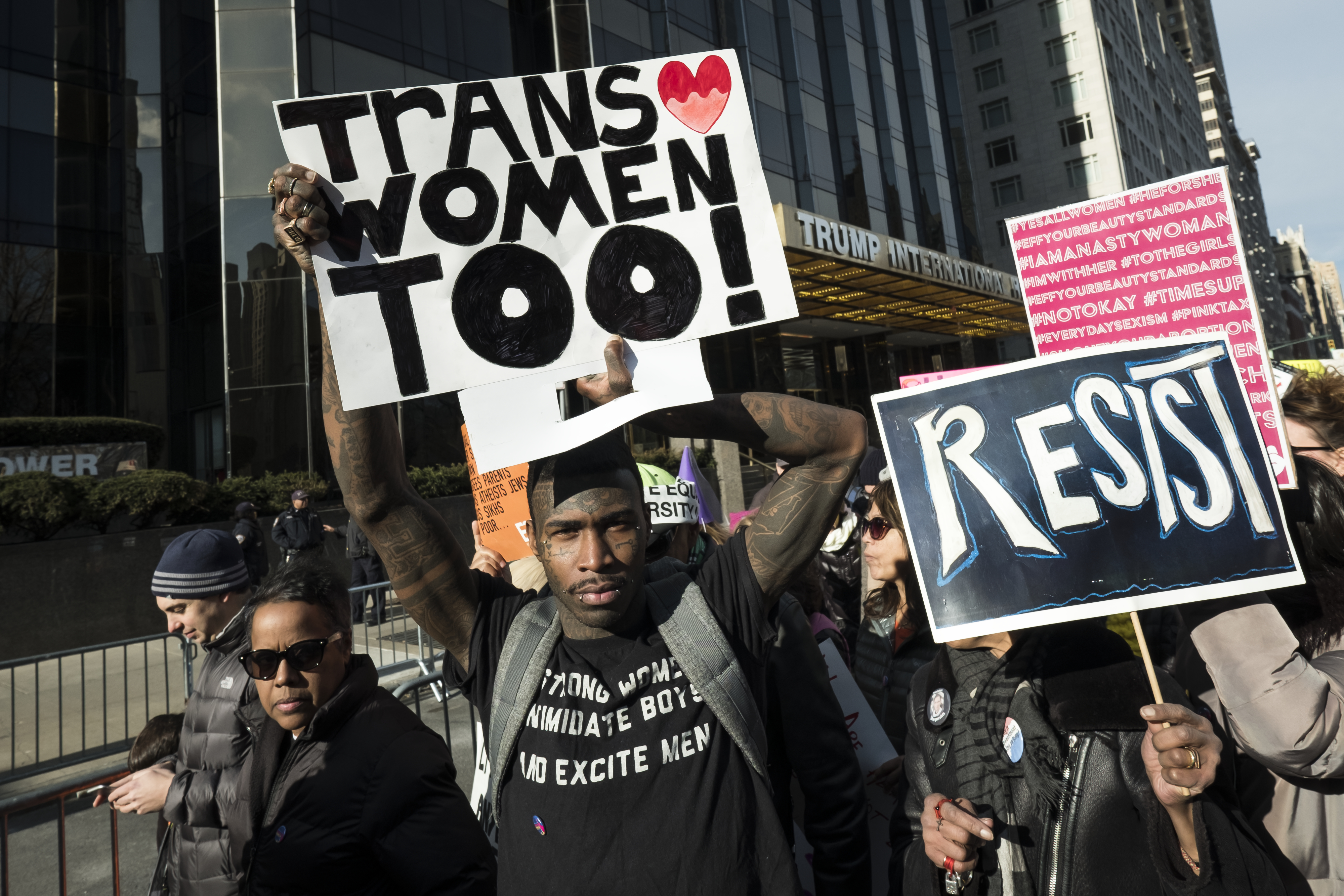 A demonstrator holds up a banner saying "Trans Women Too" and another holds a sign that says "RESIST" in front of Trump International Hotel and Tower during the second annual Women's March in the borough of Manhattan in New York City, U.S. on Saturday, January 20, 2018. CREDIT: Ira L. Black/Corbis via Getty Images