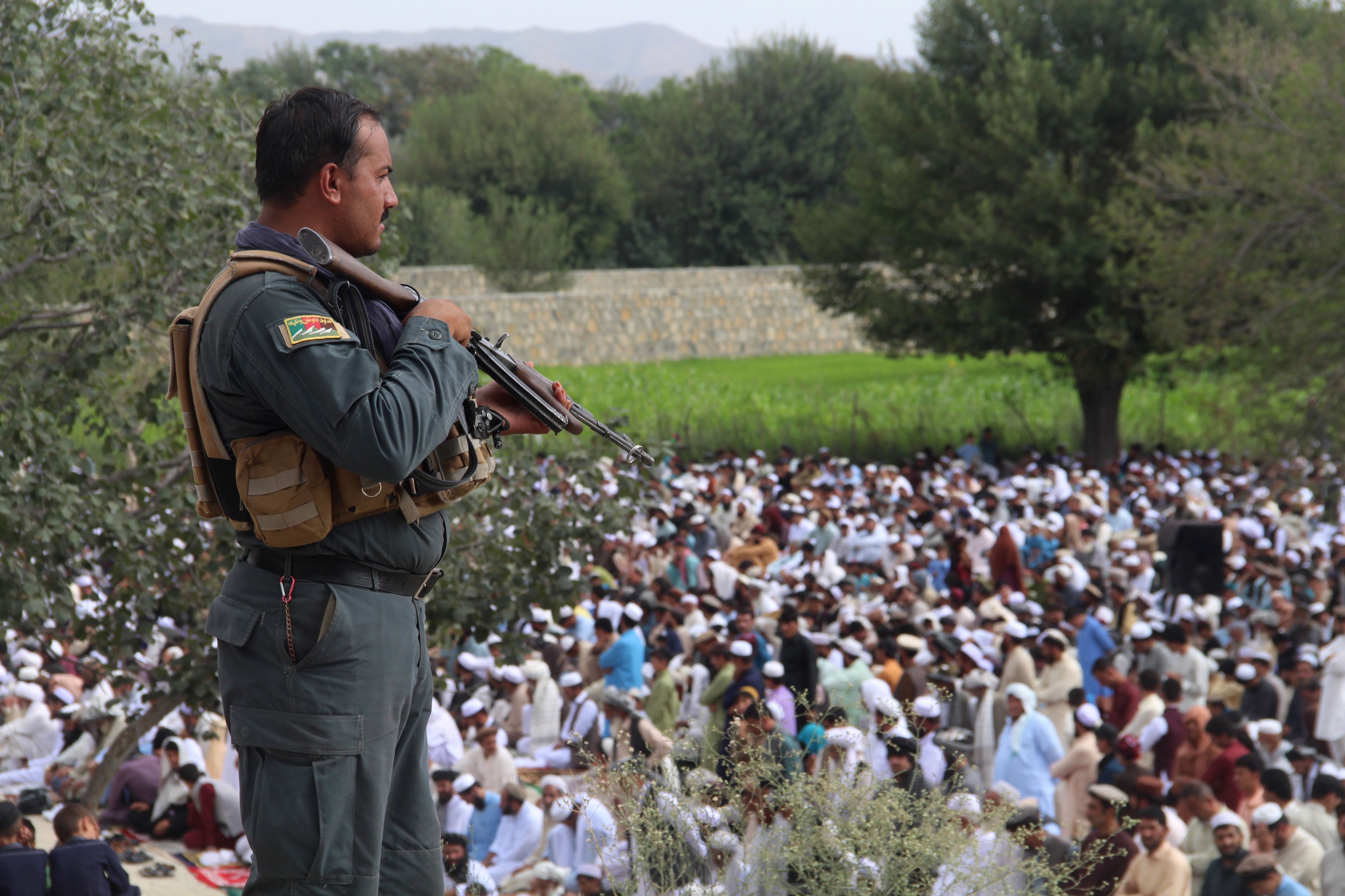 An Afghan policeman stands guard as Muslim men listen during Eid al-Adha prayers in a field in Khost province on August 11, 2019. CREDIT: NOORULLAH SHIRZADA/AFP/Getty Images)